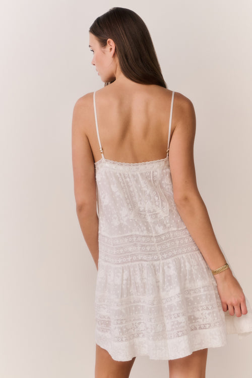 Woman wearing a white lace mini dress against a plain background