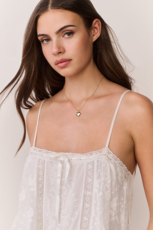 Woman wearing a white lace top and heart-shaped necklace against a plain background