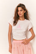 Woman wearing a white t-shirt with a pink logo and a pink skirt against a light background