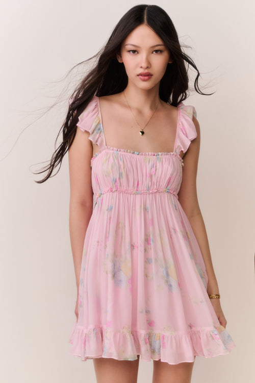Woman wearing pink floral mini dress with thin ruffle straps on a plain background
