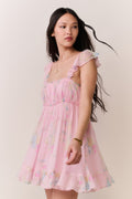 Woman wearing pink floral mini dress with thin ruffle straps on a plain background