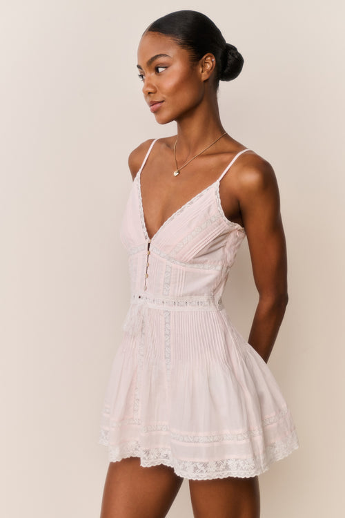 Woman wearing a light pink lace mini dress against a plain background