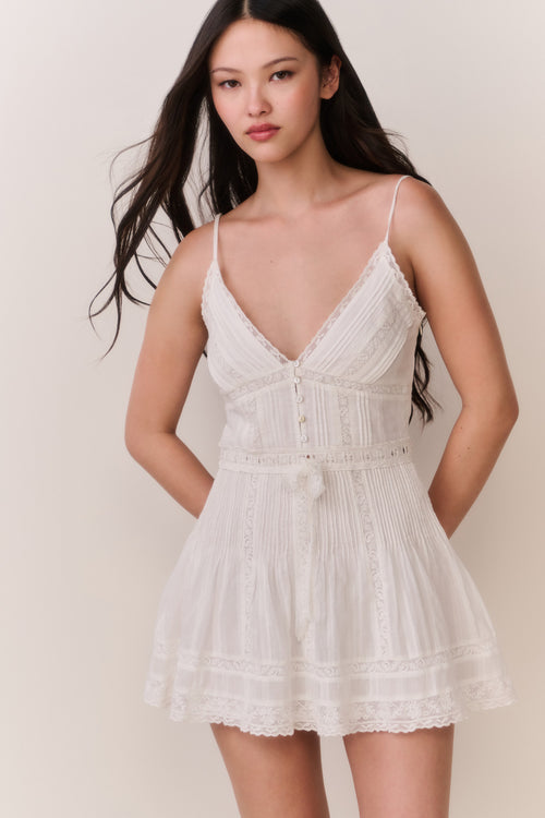 Woman wearing a white lace sleeveless dress against a plain background