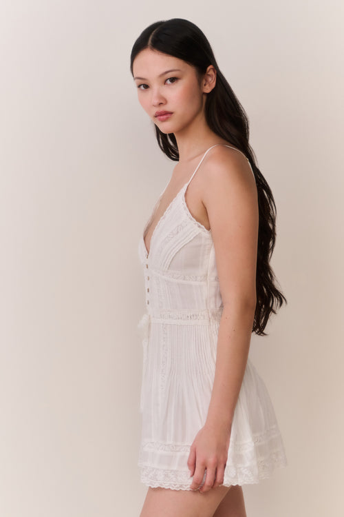 Woman wearing a white lace sleeveless dress against a plain background