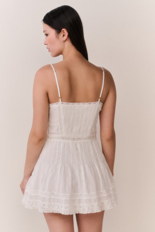 Woman wearing a white lace sleeveless dress against a plain background