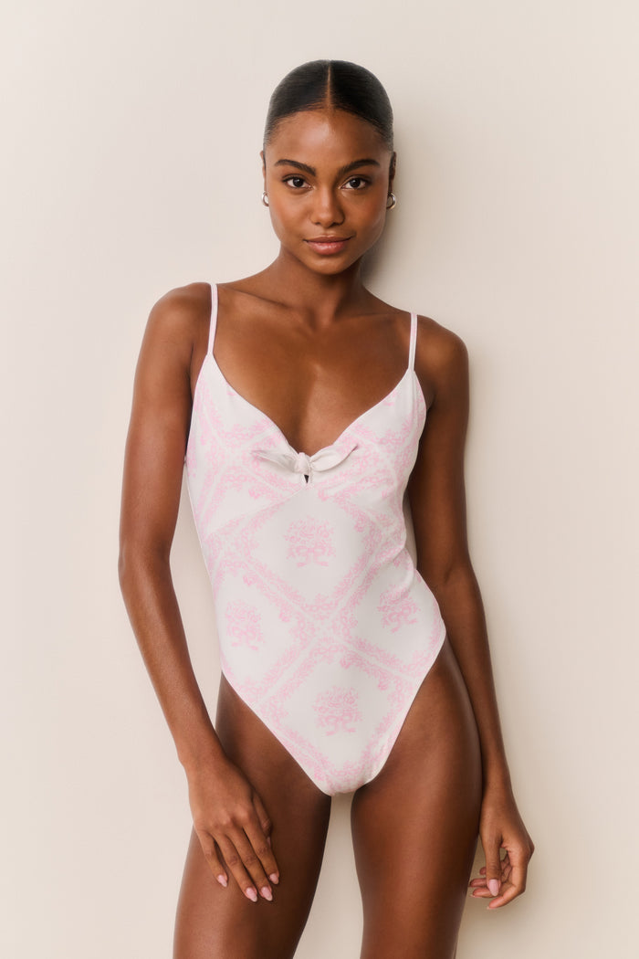 Woman wearing a pink swimsuit with thin straps against a beige background