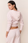 Woman wearing a light pink sweatshirt and pants against a plain background