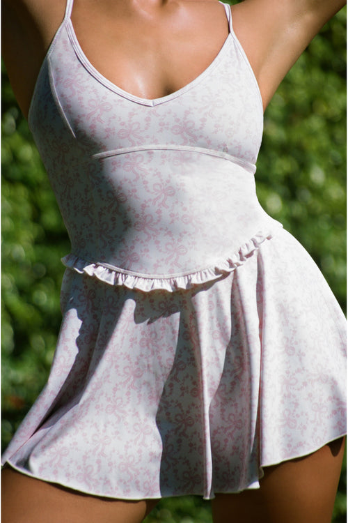 Light pink and white tennis dress with ruffled hem against a blurred green background