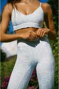 Person wearing a light blue sports bra and leggings outdoors with greenery in the background