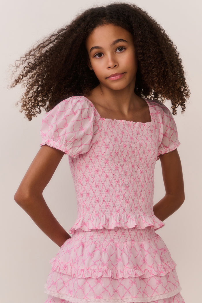 Young girl wearing a pink patterned dress against a plain background
