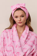 Woman wearing a pink robe and headband with a bow on a beige background