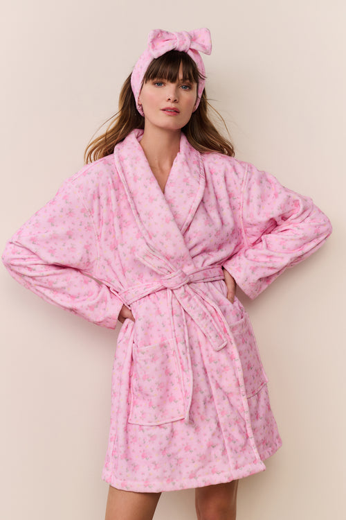 Woman wearing a pink robe and matching headband against a beige background