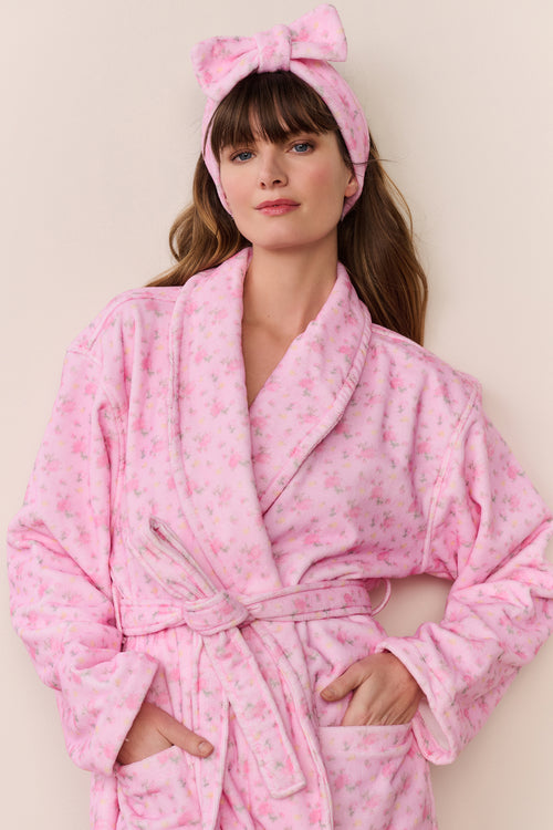 Woman wearing a pink robe and matching headband with a bow on a beige background