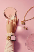Hand holding a compact mirror with jewelry on a pink background