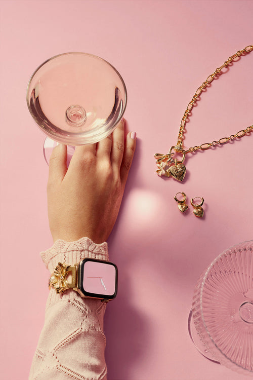 Hand holding a compact mirror with jewelry on a pink background