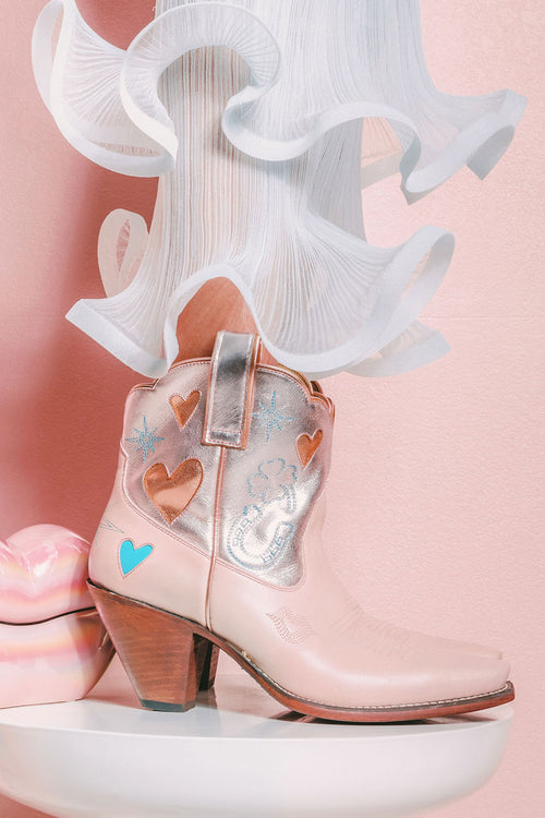 Pink cowboy boot with heart designs on a pink background
