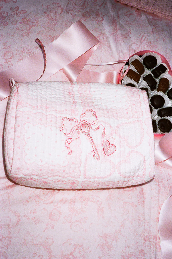 Pink cosmetic pouch with embroidered design on a pink floral background