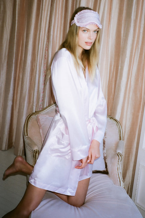 Woman in a white satin robe sitting on a chair with beige curtains in the background