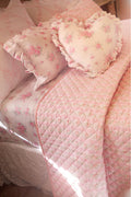 Pink quilt and pillows with floral patterns on a bed