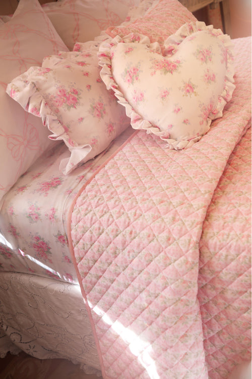 Pink quilt and pillows with floral patterns on a bed