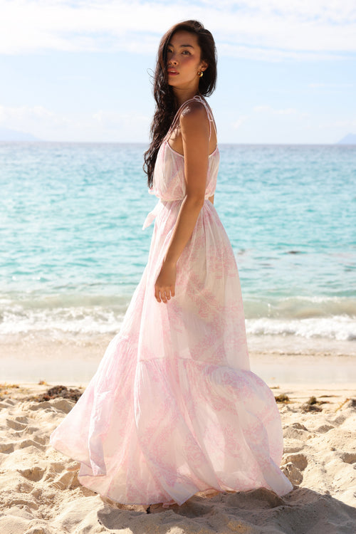 Woman in a pink dress standing on a beach with ocean in the background