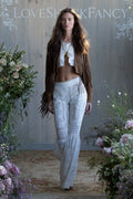 Woman in a Brown suede fringe jacket and lace white pants with floral decorations and 'LOVE SHACK FANCY' branding.