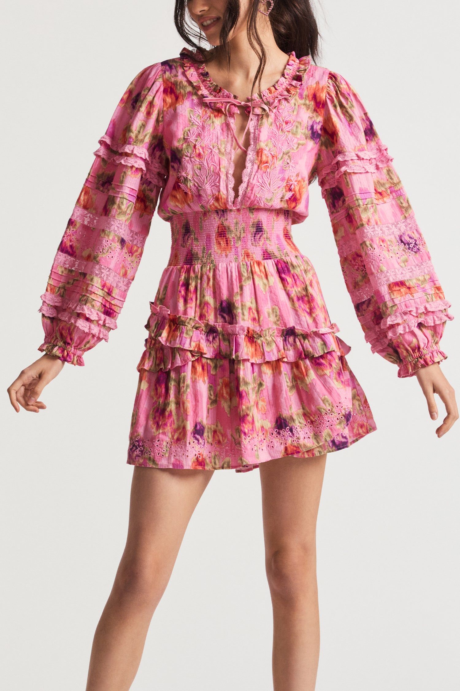 Pink mini dress with floral print with intricate embroidery and lace placements. At the center front, you can tie at the neck, ruffle detail, a smocked waist, and skirt with ruffles and embroidery around the sweep.
