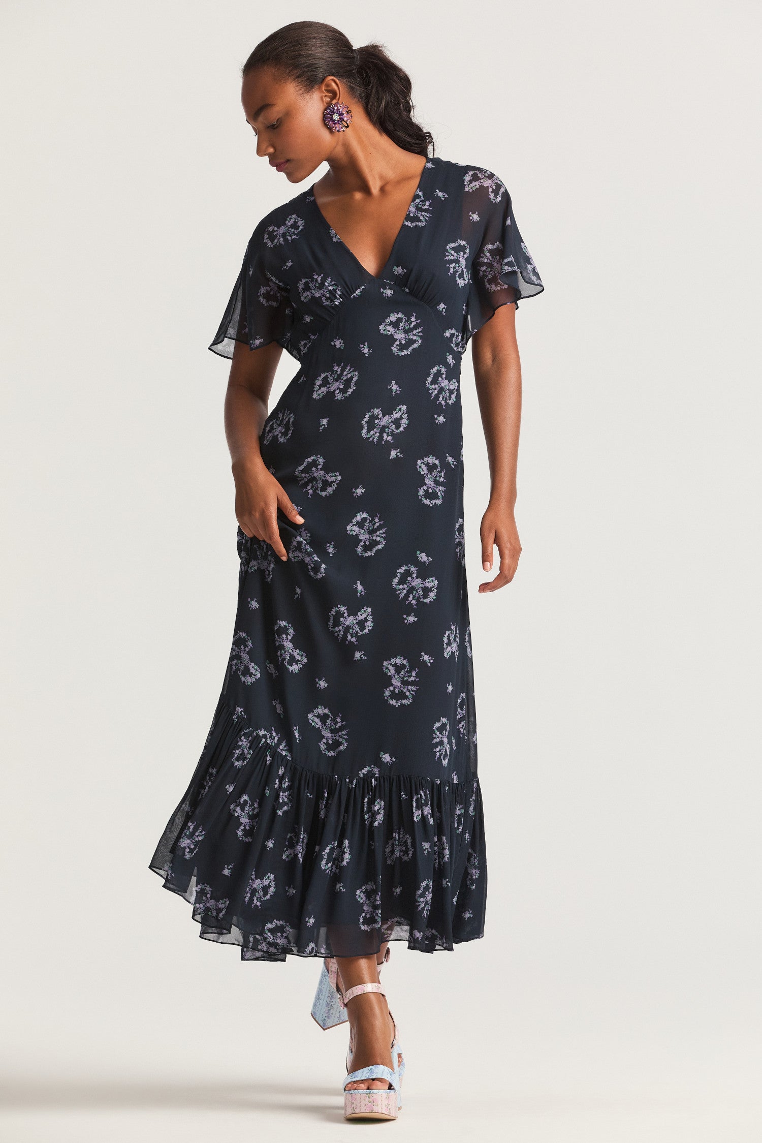 Dark blue slip midi dress, with elegant bow print on a viscose fabric. A deep v neckline with light flutter sleeves falls to a shaped waist seam that flows to a flounce skirt. 