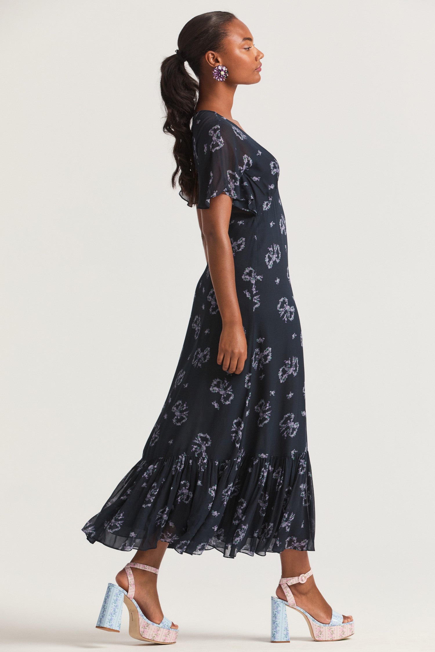 Dark blue slip midi dress, with elegant bow print on a viscose fabric. A deep v neckline with light flutter sleeves falls to a shaped waist seam that flows to a flounce skirt.
