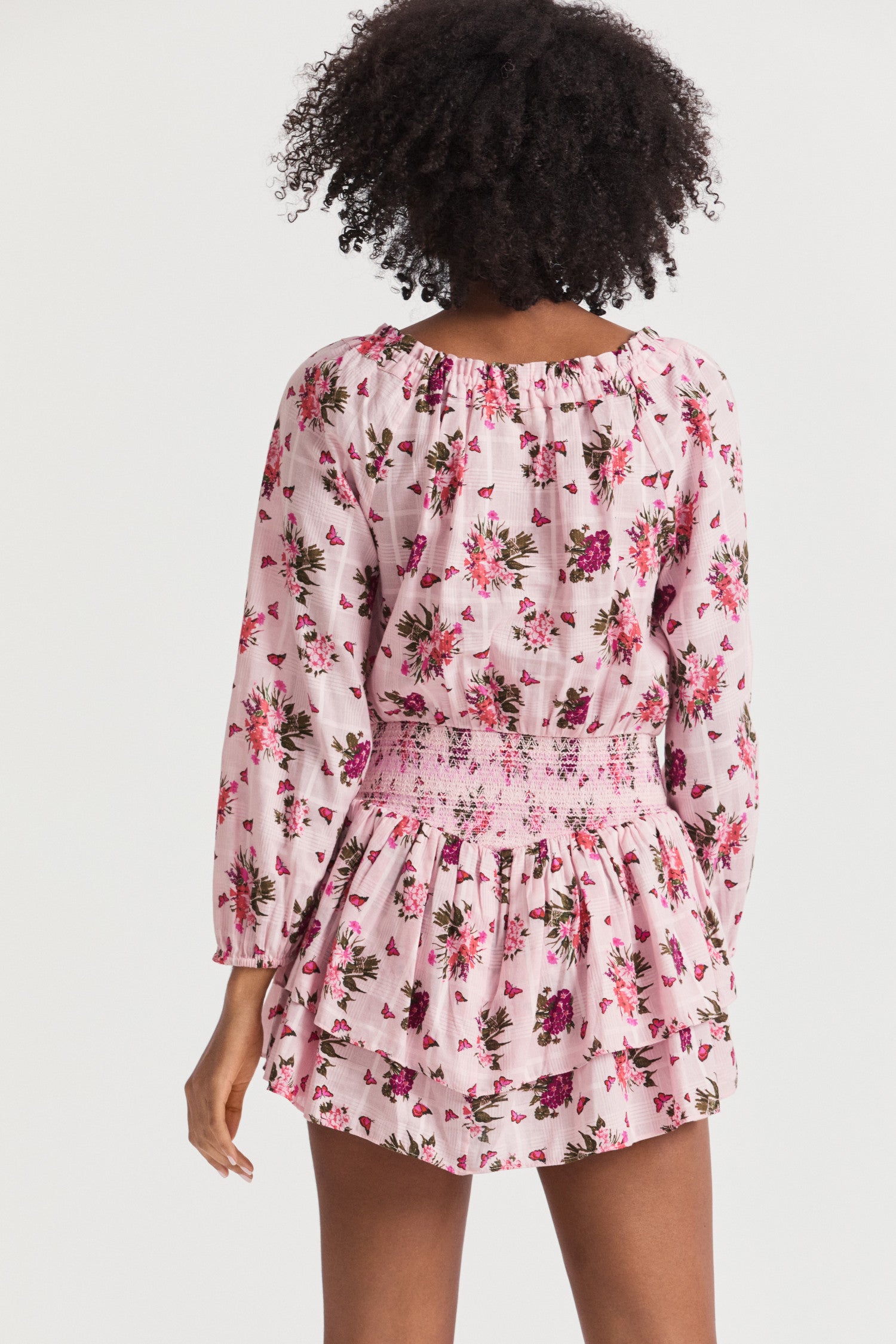 Pink mini dress with a pink floral print. Featuring an elasticated neck opening with a tie at the front, an easy bodice with a stretchy smocked waist that releases into a tiered skirt that hikes up slightly on each side.