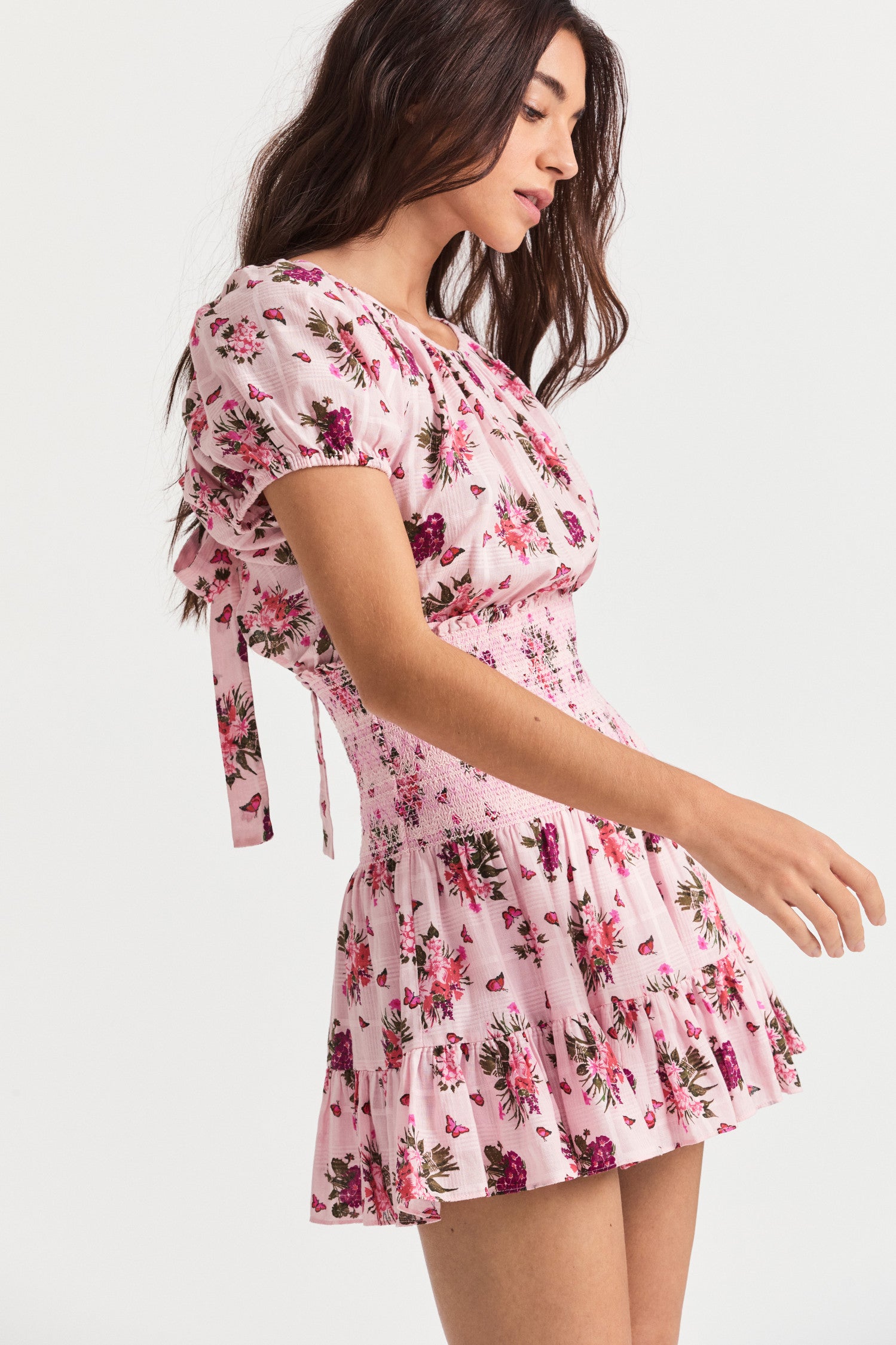 Pink floral mini dress with smocking detail, an elasticated neck opening, short puff sleeves, a flowy skirt, and a bow revealing a slightly open back. 