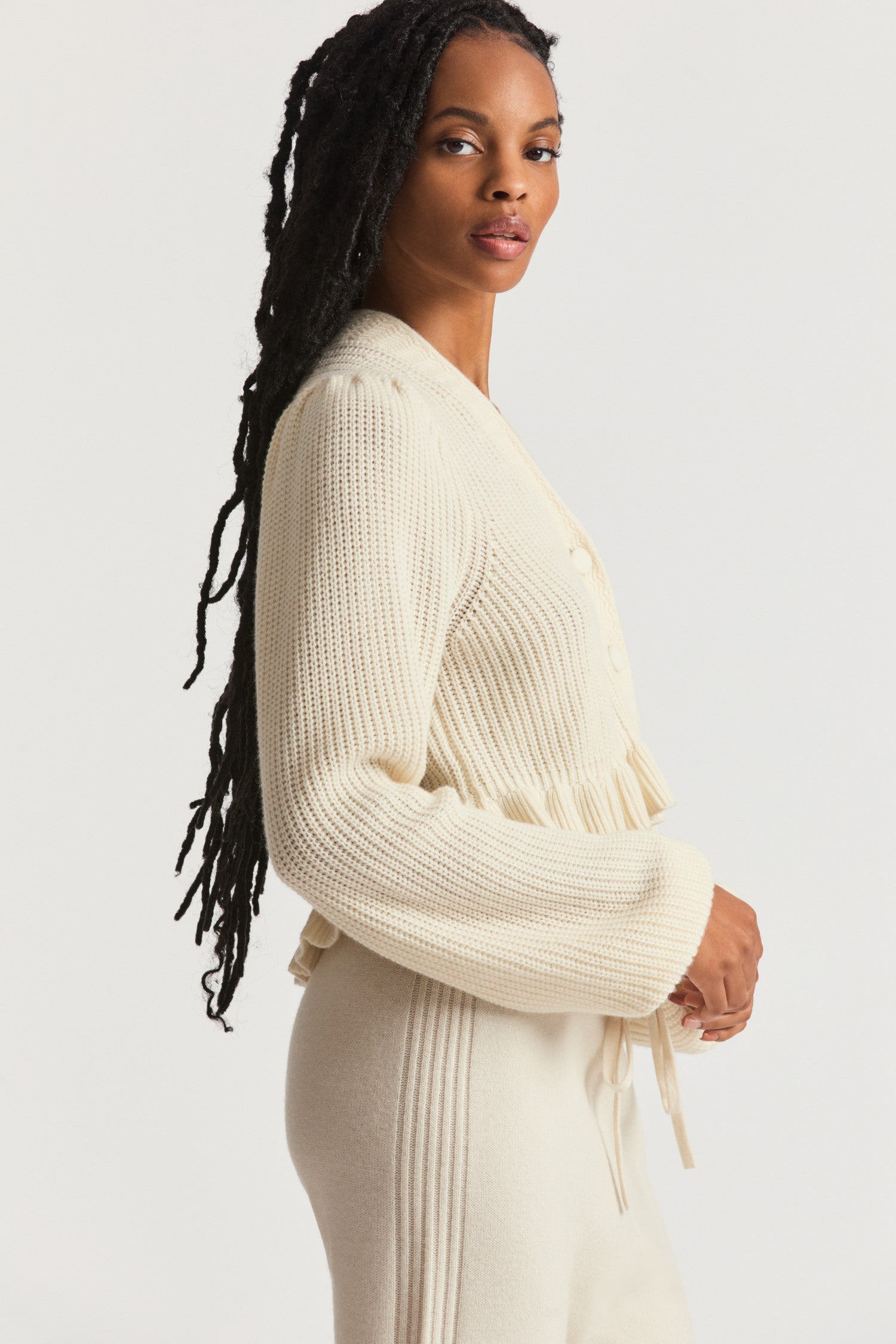 Cream cardigan in ultra-soft cashmere-wool blend with intricate ribbed knit techniques. With a v-neck that descends to three round buttons at the center front and pretty blouson sleeves. 