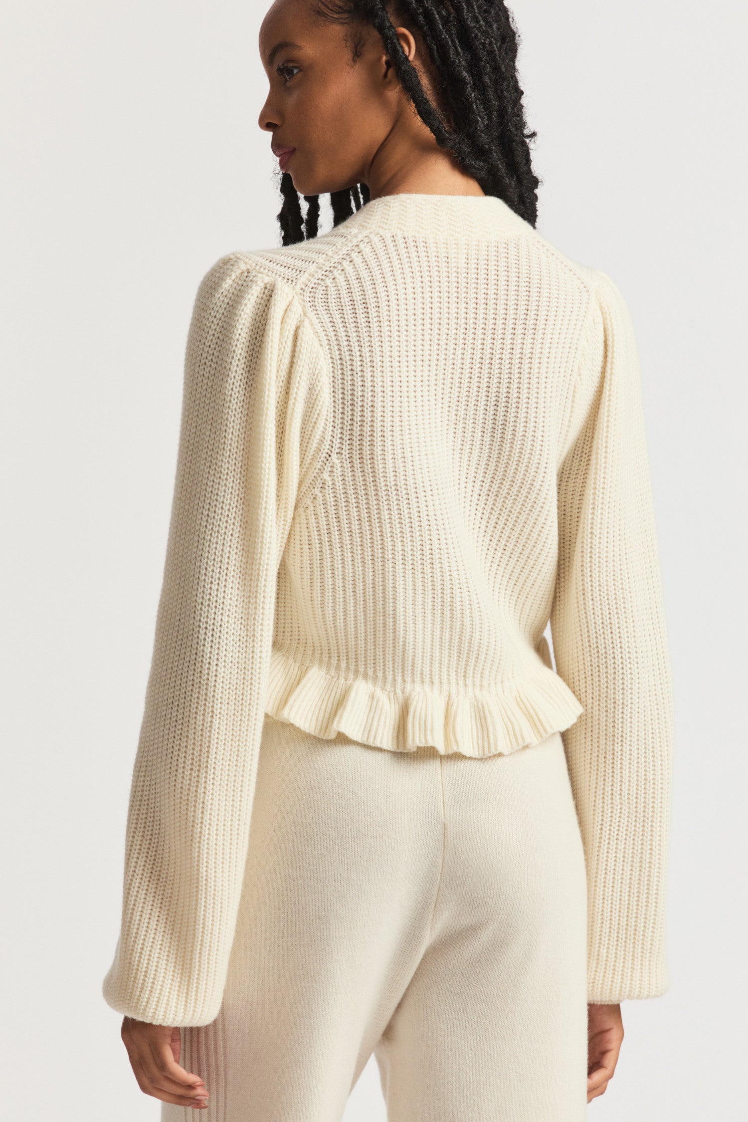 Cream cardigan in ultra-soft cashmere-wool blend with intricate ribbed knit techniques. With a v-neck that descends to three round buttons at the center front and pretty blouson sleeves. 