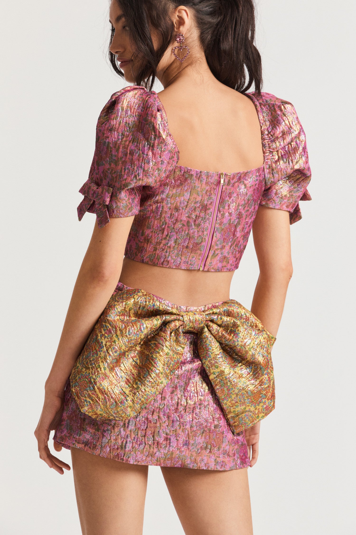 Pink micro mini skirt, low-waisted with a decadent textural crocheted fabric with luxurious floral print. Features a bow on the back in a contrasting print.