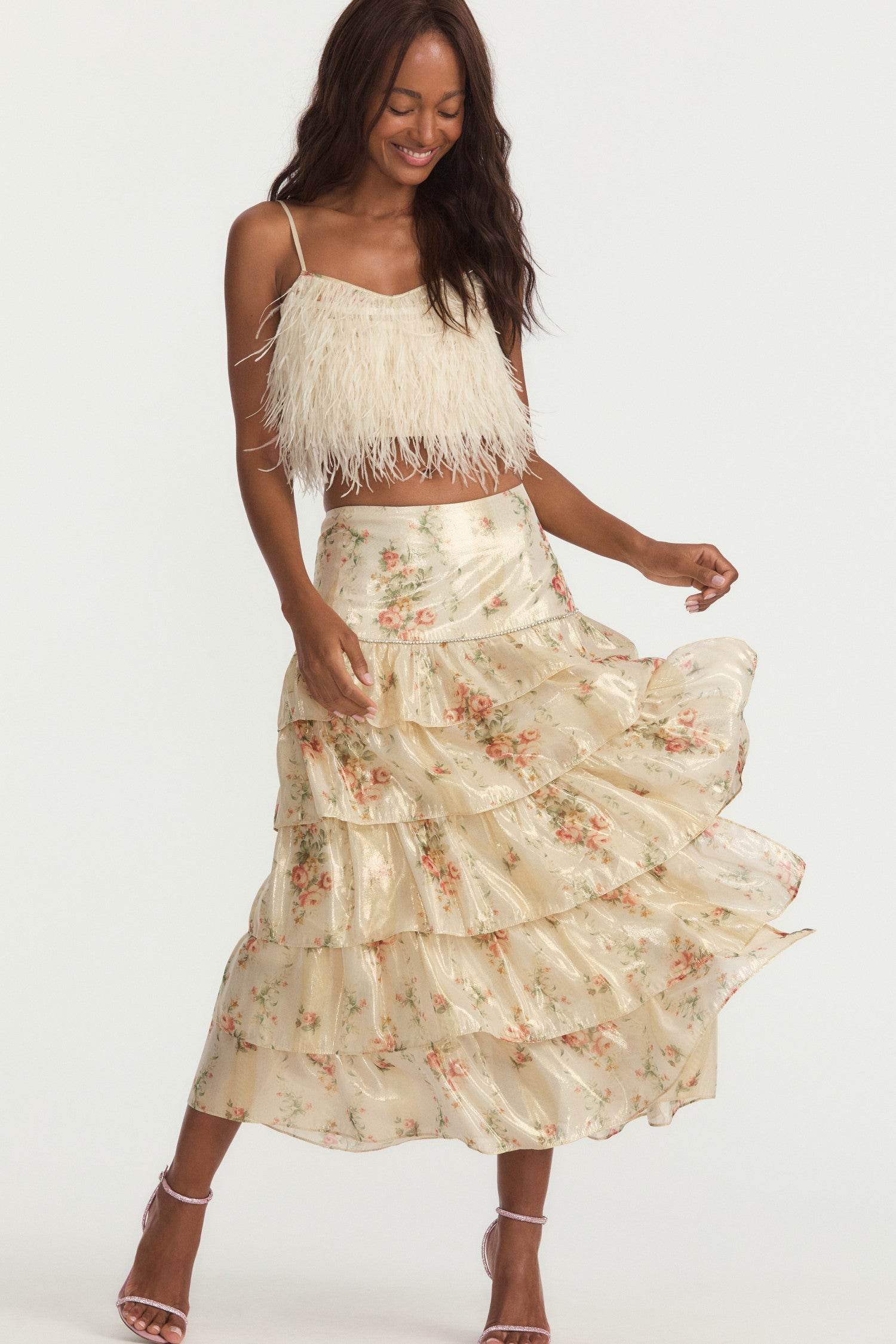 Off-white midi skirt, with floral print that paints a lurex lame fabric featuring a rhinestone trim at the flounce seam and yoke, a slit on the left, and a gold exposed metal zipper. 