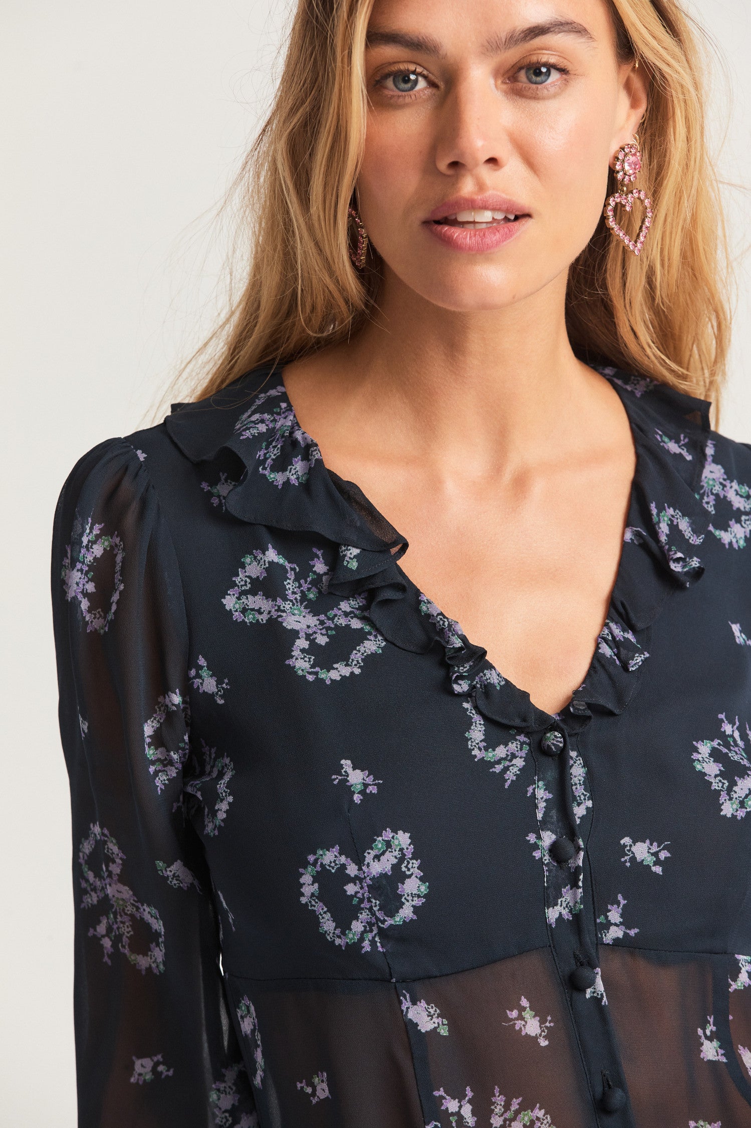 Navy blue bell long-sleeved top, with ruffles around the neck opening that falls to a modest v-neck. Slim-fit top featuring two buttons down the front. There is a sheer bottom with lining on the front and back. 