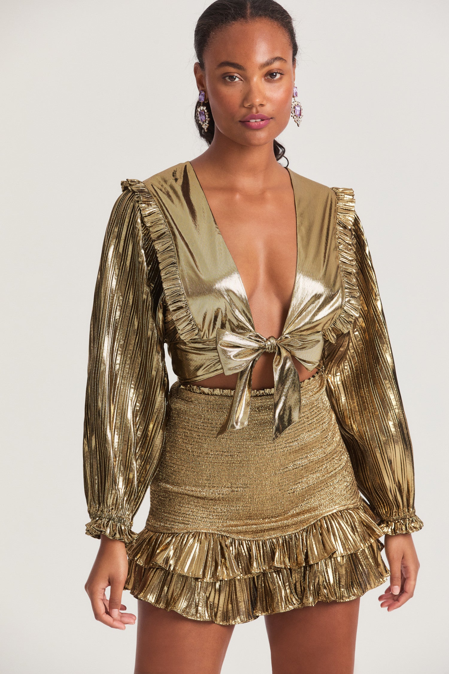 Gold crop top made of mixture of a shiny flat and pleated lame fabric. Pleated ruffles adorn the shoulders with a functional tie detail at the front. 
