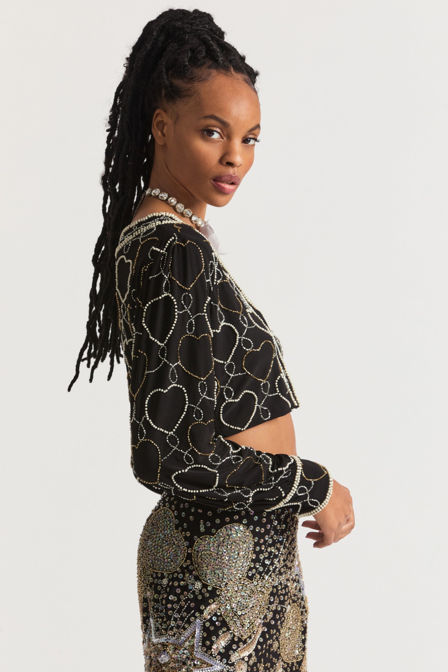 Black Crop Cardigan with heart design in iridescent silver and gold beads blended together on a stretchy crepe fabric. The collar and cuff feature delicate borders of beads.