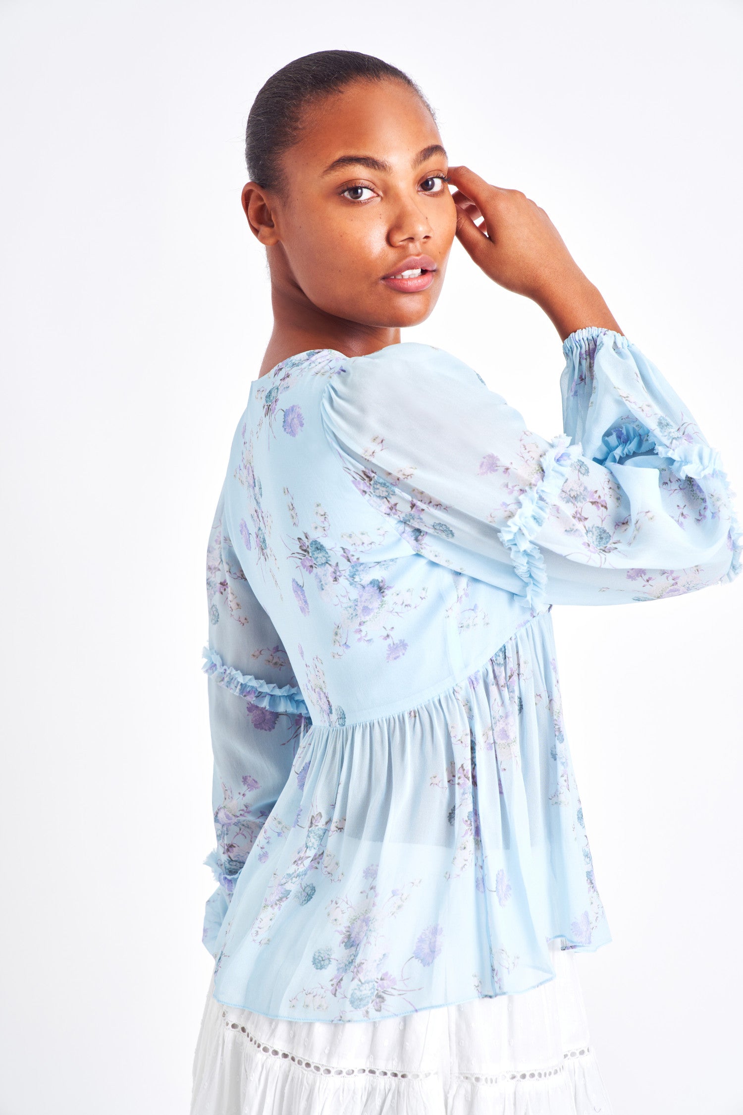 Light blue floral blouse with long ruffle sleeves, smocked shoulders, and subtle buttons down the center.