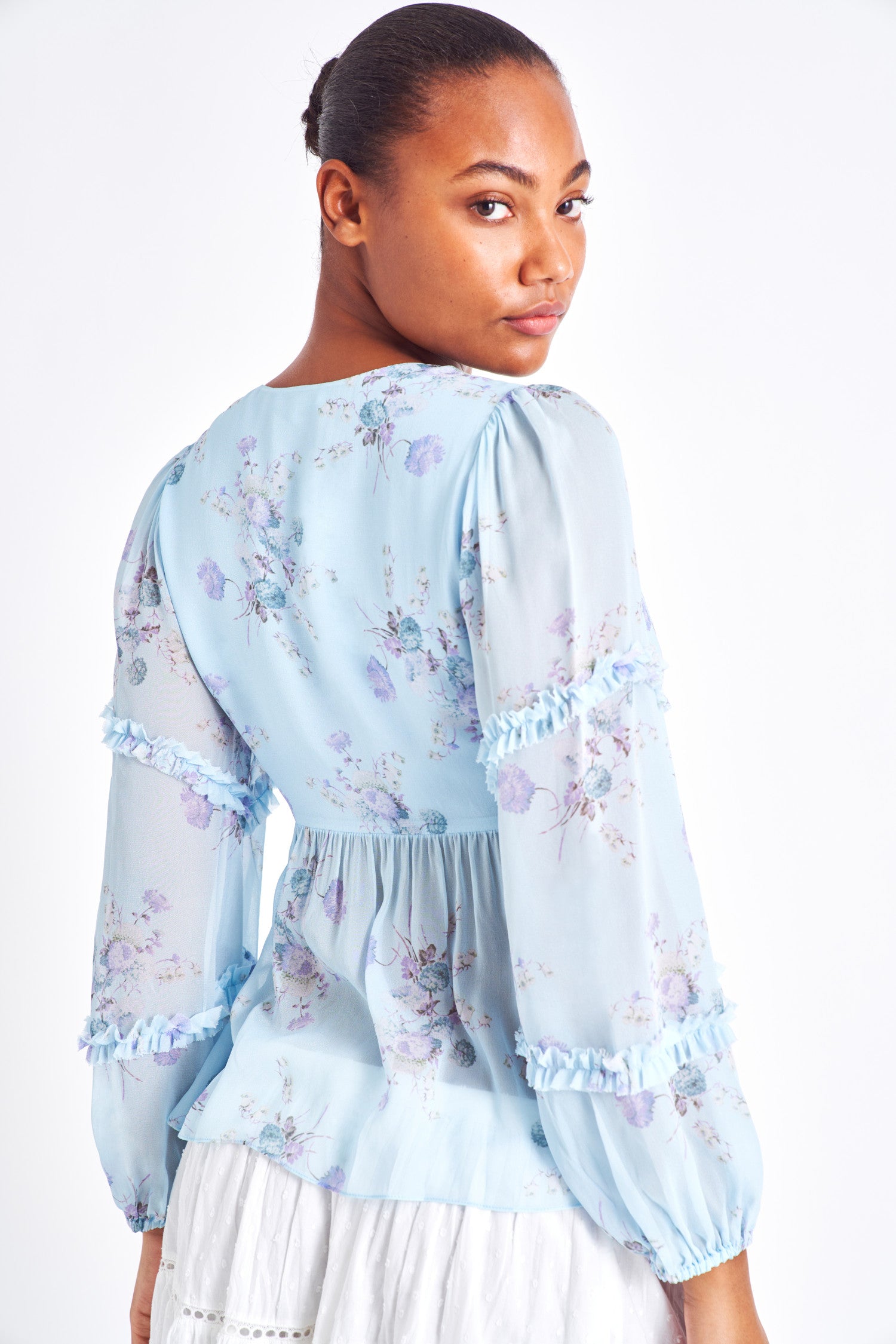 Light blue floral blouse with long ruffle sleeves, smocked shoulders, and subtle buttons down the center.